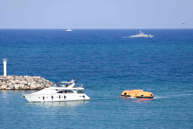 A rescue raft is towed into port as Turkish vessels are pictured off the port of Kyrenia in the self-proclaimed Turkish Republic of Northern Cyprus (TRNC), recognised only by Turkey, in the north of the divided Mediterranean island of Cyprus on August 30, 2026, during search and rescue operations following a ferry capsizing. At least six people died when a ferry capsized off Northern Cyprus on August 30, the head of the local government said, in a preliminary toll to Turkish media. The vessel had been carrying a total of 267 people when it rolled over shortly after leaving port, according to Turkish state news agency Anadolu. (Photo by Birol BEBEK / AFP)