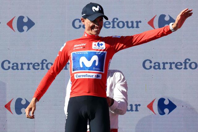 Team Movistar's Spanish rider Enric Mas is helped to put on the overall leader's red jersey as he celebrates on the podium after winning the 9th stage of the Vuelta a Espana 2026 cycling tour, a 187,4 km race between Villajoyosa and Alto de Aitana in Confrides, on August 30, 2026. (Photo by Josep LAGO / AFP)