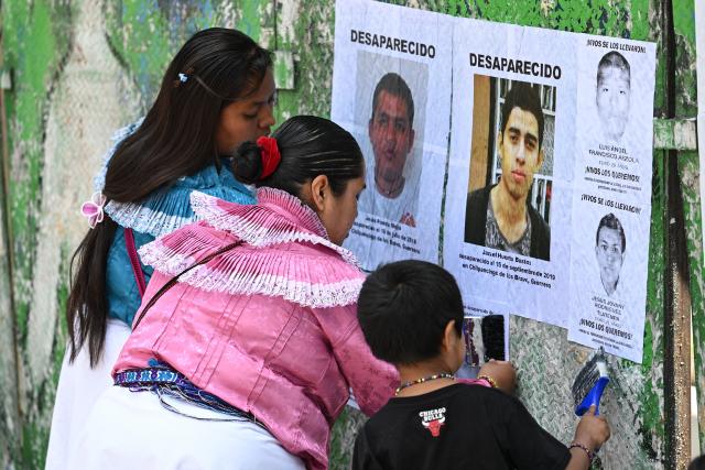 Members of collectives of mothers and families searching for missing persons paste posters with pictures of their missing relatives during an event to commemorate the International Day of the Victims of Enforced Disappearances at the so-called "Glorieta de las y los Desaparecidos" (Roundabout of the Disappeared) in Mexico City on August 30, 2026. (Photo by Yuri CORTEZ / AFP)