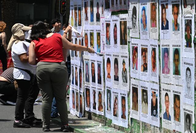 Members of collectives of mothers and families searching for missing persons paste posters with pictures of their missing relatives during an event to commemorate the International Day of the Victims of Enforced Disappearances at the so-called "Glorieta de las y los Desaparecidos" (Roundabout of the Disappeared) in Mexico City on August 30, 2026. (Photo by Yuri CORTEZ / AFP)