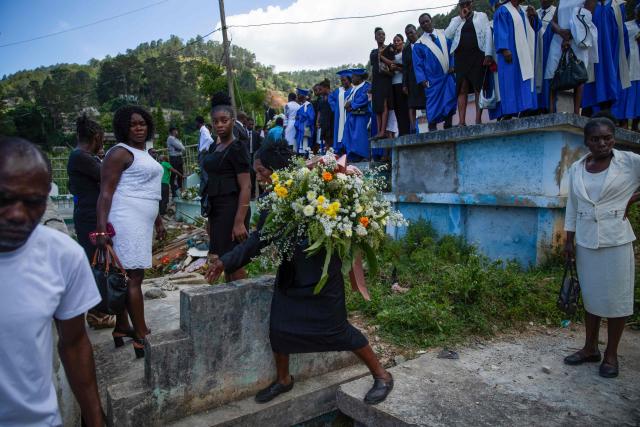 A woman carries flowers during a collective funeral for more than twenty people killed by armed gangs last week in Kenscoff, a neighborhood near Port-au-Prince, on August 30, 2026. Gang members attacked displaced people huddling inside a church near Haiti's capital, killing around 40, some of them execution-style, the mayor told AFP on August 24. (Photo by Clarens SIFFROY / AFP)