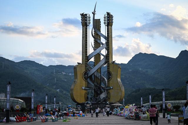 This photo taken on July 26, 2026 shows people walking past a giant installation of guitars at the Guitar Cultural Plaza in Zheng'an, in southwestern China's Guizhou Province. The town of Zheng'an in the southwest province of Guizhou produces one in every seven of the instruments sold worldwide -- but a decade ago, it had no guitar-making industry to speak of at all. (Photo by Jade GAO / AFP) / To go with AFP story 'China-Economy-Trade-Manufacturing-Music', Reportage by Rita QIAN