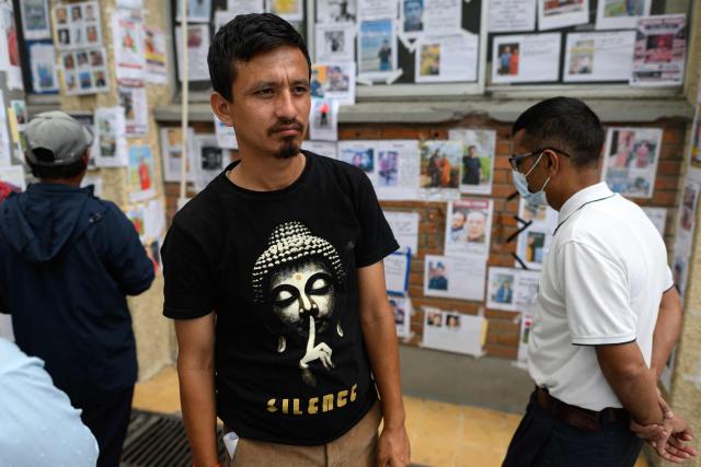 A man wearing a Buddha-themed shirt walks past a wall adorned with photographs of missing persons in the aftermath of flash floods, at the Tribhuvan University Teaching hospital in Kathmandu on August 31, 2026. Nepal was burying on August 31 some of the hundreds of bodies retrieved after a deadly, tsunami-like flood crashed through the Himalayan region, sweeping away villages and leaving thousands still missing. Distraught families have packed rescue stations and hospitals in search of their missing relatives, while others have faced the grim task of identifying bodies at overflowing morgues. (Photo by MANAN VATSYAYANA / AFP)