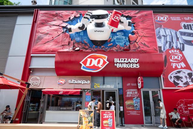 People stand and sit in front of a 24-hour DQ Blizzard & Burgers restaurant in Shanghai on August 31, 2026. The store, jointly made by AI robot company Sharpa and Dairy Queen, opened on August 29 in Shanghai’s Jing’an district. (Photo by CN-STR / AFP) / China OUT