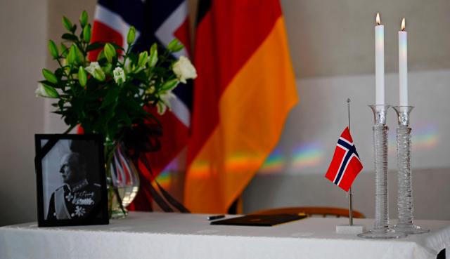 A portrait of late Norwegian King Harald V adorned with a black mourning ribbon is displayed alongside flowers, lit candles, a Norwegian flag and a book of condolences, in front of Norwegian and German flags, at the Royal Norwegian Embassy in Berlin, on August 31, 2026. King Harald V of Norway, who died on August 28, 2026 aged 89, remained a unifying figure in his country until the very end, a pillar of stability amid a string of family scandals that tarnished the final years of his reign. (Photo by Tobias SCHWARZ / AFP)