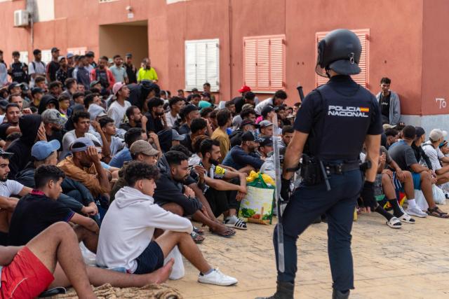 Spain's National Police officers stand as migrants wait on the sidewalk before being registered in Loma Colmenar district of Ceuta on August 31, 2026. Tensions remain high in the territory of 80,000 inhabitants since tens of thousands of people crossed into Ceuta from Morocco over several days in July, triggering a Europe-wide migrant alert. Spanish Prime Minister said the rush of migrants to the Spanish enclave was still under investigation, though he ruled out any responsibility on the part of Moroccan authorities. (Photo by Antonio Sempere / AFP)