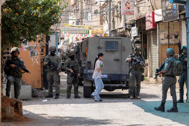 A Palestinian girl carrying a notebook walks past Israeli army soldiers and armoured vehicles during an Israeli military operation at the Balata camp for Palestinian refugees, east of Nablus in the Israeli-occupied West Bank, on August 31, 2026. Violence has surged in the West Bank, which Israel has occupied since 1967, since the start of the war in Gaza sparked by Hamas's October 2023 attack on Israel. (Photo by JAAFAR ASHTIYEH / AFP)