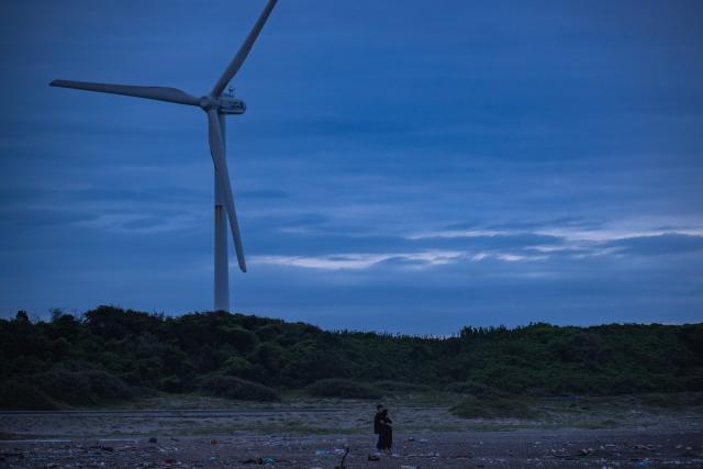 A couple visits Nikkawahama Beach as a wind turbine is seen in the background in Kamisu city, Ibaraki prefecture on August 31, 2026. (Photo by Philip FONG / AFP)