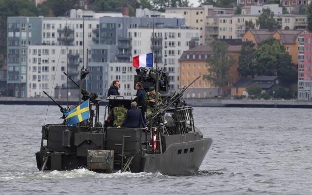 French President Emmanuel Macron (L) and Swedish Prime Minister Ulf Kristersson travel aboard a Swedish Navy CB90 fast assault craft in Stockholm, Sweden, on August 31, 2026, ahead of a bilateral meeting and the signing of a 4.3-billion-euro contract for Sweden’s acquisition of four French-built defence and intervention frigates (FDI). (Photo by Ludovic MARIN / AFP)