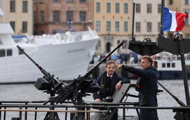 French President Emmanuel Macron (R) and Swedish Prime Minister Ulf Kristersson stand aboard a Swedish Navy CB90 fast assault craft in Stockholm, Sweden, on August 31, 2026, ahead of a bilateral meeting and the signing of a 4.3-billion-euro contract for Sweden’s acquisition of four French-built defence and intervention frigates (FDI). (Photo by Ludovic MARIN / AFP)