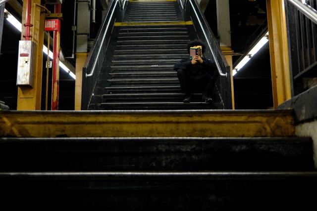 A man reads a book as he sits on the stairs of the 145th Street subway station in the middle of the night in the Manhattan borough of New York City on August 31, 2026. (Photo by CHARLY TRIBALLEAU / AFP)