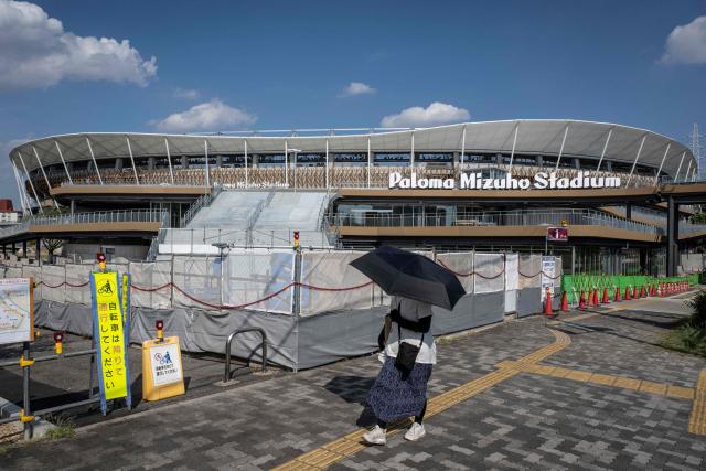 (FILES) This picture taken on September 7, 2025 shows a woman shielding herself from the hot sun with an umbrella as she walks past the Nagoya City Mizuho Park Athletic Stadium, the venue for track and field and marathon competitions in the upcoming 2026 Aichi-Nagoya Asian Games in Nagoya, Aichi prefecture. (Photo by Yuichi YAMAZAKI / AFP)