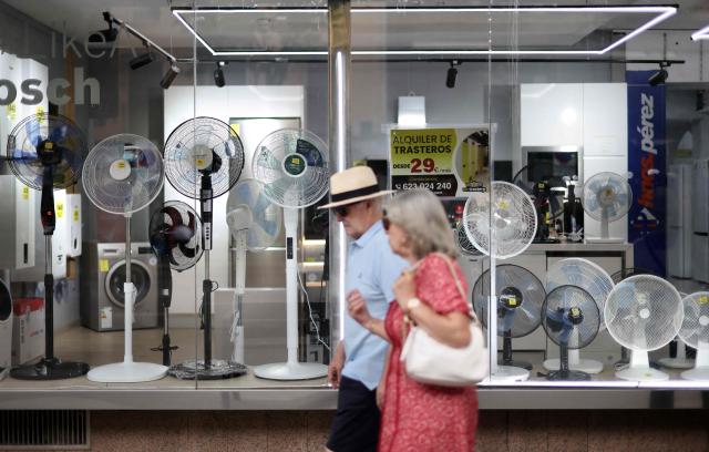 (FILES) People walk past the window display of a shop selling fans during a heatwave in Madrid, on June 25, 2026. Spain registered more than 5,000 heat-related deaths from June to August, data from a public health institute showed on August 31, 2026, a record since the start of its statistics in 2015. (Photo by Thomas COEX / AFP)