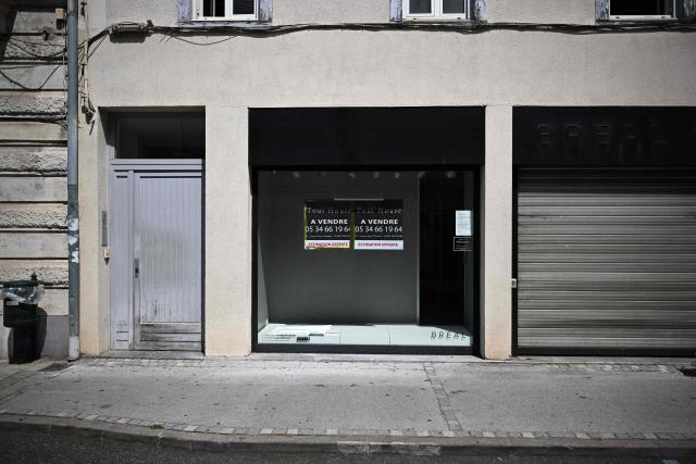 This photograph shows the storefront of a closed business in Saint-Gaudens, where commercial vacancy has increased over the past ten years on July 29, 2026. 'For sale', 'to let', 'potential to convert into a home': the streets of Saint-Gaudens' old town are dotted with closed-down commercial premises, whilst this town of just over 12,000 inhabitants at the foot of the Pyrenees fears losing its paper pulp mill and the hundreds of jobs it provides. "Watchmaker and jeweller", "quick alterations", "hairdresser", "optician"  these are the signs visible on some of the abandoned shop fronts, giving a clue as to what sort of business once occupied the premises. In other cases, there is no trace left of the former business. Some shop windows are even completely covered by posters of all kinds, including some dating back several years, such as one calling for a protest against the 2023 pension reforms. (Photo by Lionel BONAVENTURE / AFP)