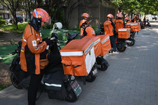 Food delivery riders wait for orders while parked on a street in Beijing on September 2, 2026. (Photo by Pedro PARDO / AFP)