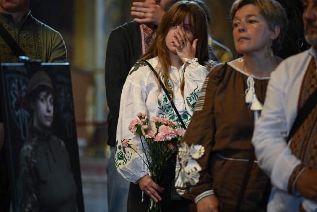 Relatives and friends mourn next to a portrait of the late paramedic of the Ukrainian volunteer medical battalion Hospitallers, Eva Roiter, 25, during the funeral service in Saint Michael's Golden-Domed Cathedral in Kyiv on September 2, 2026, amid the Russian invasion of Ukraine. (Photo by Genya SAVILOV / AFP)