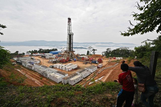 (FILES) A woman and children look at Bolivia's state-run oil company Yacimientos Petrolíferos Fiscales Bolivianos (YPFB) Mayaya Centro-X1 natural gas field in Alto Beni, Caranavi Province, Bolivia, on July 23, 2024. The Bolivian government ordered temporary intervention of the state-owned oil company YPFB in order to "restore efficiency" to its management, amid a fuel supply crisis, according to a decree published in the official gazette on September 2, 2026. (Photo by Aizar RALDES / AFP)