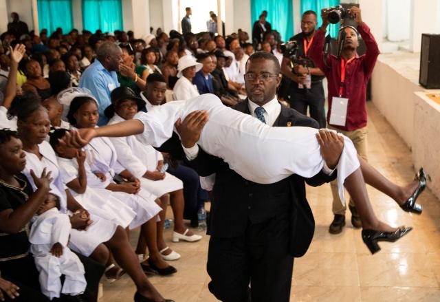 An overwhelmed woman is carried out of a collective funeral service for more than twenty people killed by armed gangs last week in Kenscoff, a neighborhood near Port-au-Prince, on September 2, 2026. Gang members attacked displaced people huddling inside a church near Haiti's capital, killing around 40, some of them execution-style, the mayor told AFP on August 24. (Photo by Clarens SIFFROY / AFP)