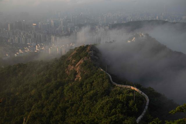 Hikers are seen on Beom Rock as they enjoy the view of the skyline and Seoul City Wall on Inwangsan Mountain in Seoul on September 3, 2026. (Photo by Lillian SUWANRUMPHA / AFP)