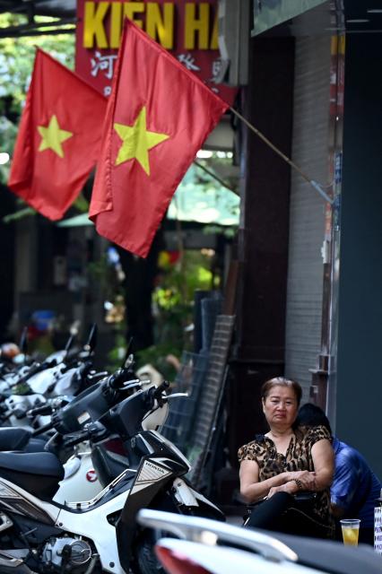 A woman sits drinking water beneath Vietnamese flags in Hanoi on September 3, 2026. (Photo by Nhac NGUYEN / AFP)