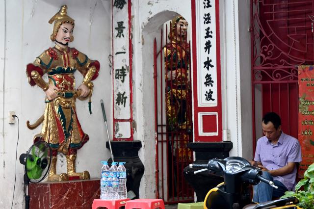 A man sits using his phone at the entrance of a temple in Hanoi on September 3, 2026. (Photo by Nhac NGUYEN / AFP)