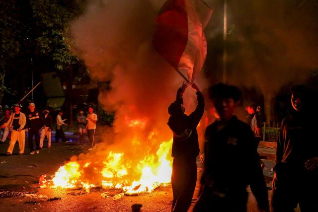 (FILES) Protesters walk past a burning police motorcycle as a man waves a flag of Indonesia during a demonstration urging lawmakers to immediately pass an asset forfeiture law for corrupt officials outside the Parliament building in Jakarta on August 27, 2026. Disinformation about ongoing anti-government protests in Indonesia has inundated social media in what investigators say is a coordinated attempt to spread propaganda about the one-year-old movement. (Photo by AZWAR IPANK / AFP)