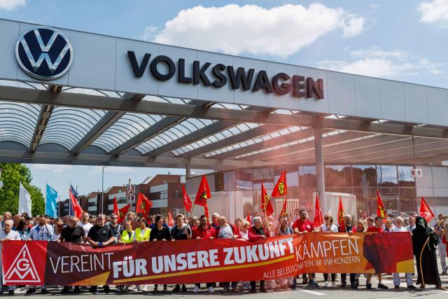 (FILES) Employees of German car maker Volkswagen (VW) wave flags and display banners as they take part in a rally called by German trade union IG Metall to protest against restructuring and mass job cut plans at the VW plant in Zwickau, eastern Germany on July 9, 2026. German car giant Volkswagen said on September 3, 2026 that management and unions had agreed to cut a further 50,000 jobs by the end of the decade, bringing total job losses to 100,000. "It is essential to systematically align workforce levels with economic realities," the 10-brand group said in a statement, adding the firm had approved a plan which involved "the reduction of around 50,000 jobs" on top of the 50,000 already agreed. (Photo by Jens SCHLÜTER / AFP)
