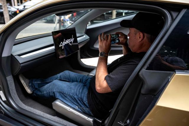 A man takes a photo inside a Tesla's "Cybercab" as it's displayed in downtown Austin, Texas, on September 3, 2026. Tesla is launching the "Cybercab" which is a taxi with no steering wheel or pedals, designed purely for autonomy. (Photo by RONALDO SCHEMIDT / AFP)