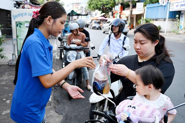 A woman buys coffee in a plastic bag from a coffee stall in Phnom Penh on September 4, 2026. (Photo by TANG CHHIN Sothy / AFP)