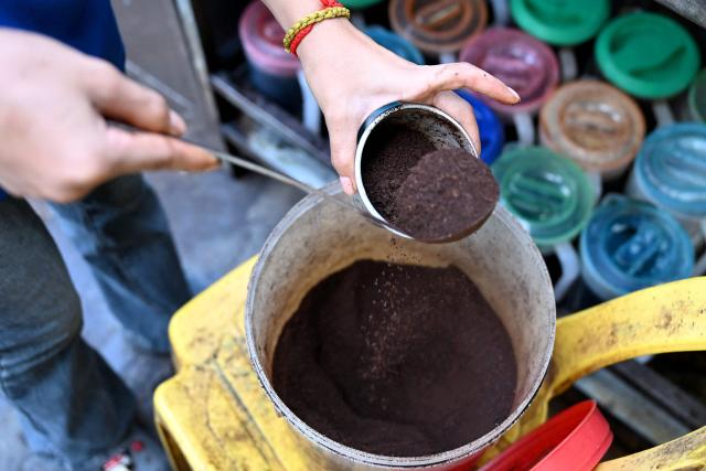 A worker scoops coffee powder into a metal filter at a coffee stall in Phnom Penh on September 4, 2026. (Photo by TANG CHHIN Sothy / AFP)