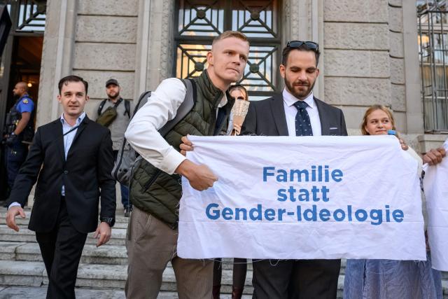 Leading figures of the Swiss far-right group Junge Tat, Manuel Corchia (L) and Tobias Lingg (C) pose next to a banner reading in German "Family instead of gender ideology" as they arrive at Zurich District Court for their trial, in Zurich, on September 4, 2026. Six people from the far-right group Junge Tat appeared before the Zurich District Court, accused of hatred-related offenses, coercion, rioting, property damage and trespassing. The group's two main leaders face up to six months in prison. (Photo by Fabrice COFFRINI / AFP)