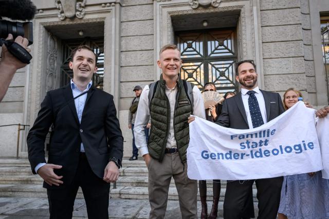 Leading figures of the Swiss far-right extremist group Junge Tat, Manuel Corchia (L) and Tobias Lingg (C) pose next to a banner reading in German "Family instead of gender ideology" as they arrive at Zurich District Court for their trial, in Zurich, on September 4, 2026. Six people from the far-right group Junge Tat appeared before the Zurich District Court, accused of hatred-related offenses, coercion, rioting, property damage and trespassing. The group's two main leaders face up to six months in prison. (Photo by Fabrice COFFRINI / AFP)