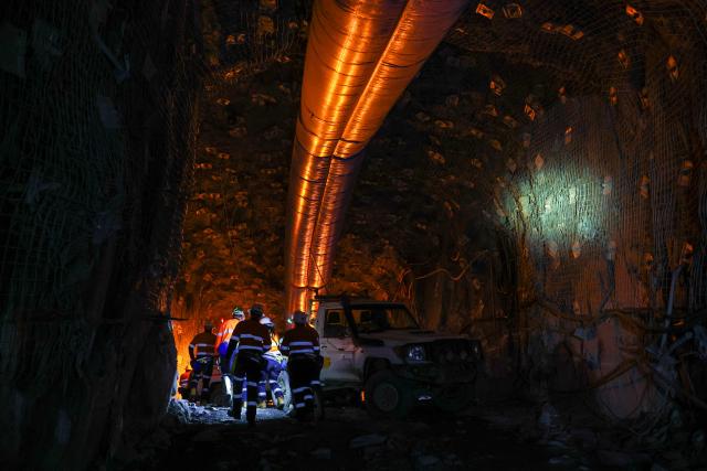 Workers and officials walk through the development drive created by a multi-purpose rock drilling machine known as a ‘jumbo’ in the underground CSA Cobar copper mine, operated by Harmony Gold Mining company, located north of the New South Wales town of Cobar on September 4, 2026. (Photo by DAVID GRAY / AFP)