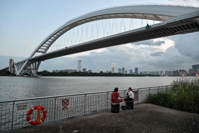 People sit next to the Huangpu river in Shanghai on September 4, 2026. (Photo by HECTOR RETAMAL / AFP)