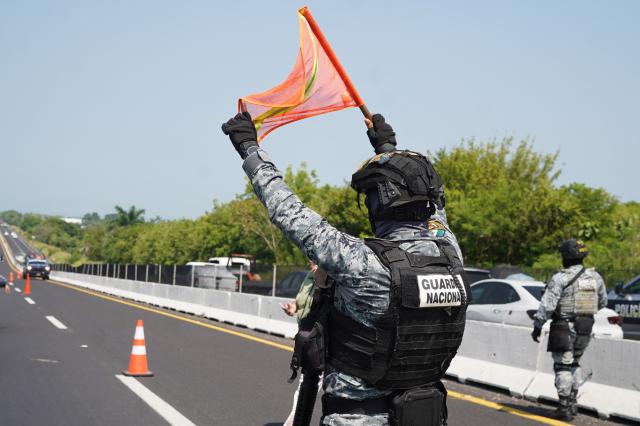 A National Guard member holds a warning flag near the scene where the body of Morena federal deputy Zenyazen Escobar was found inside a black Mercedes-Benz on the Veracruz-Xalapa highway near La Gloria, Veracruz state, Mexico, on September 4, 2026. The body of a Mexican federal lawmaker was found with a gunshot wound on a highway in the state of Veracruz, authorities said on September 4. Zenyazen Escobar was found inside his vehicle with a firearm nearby, the state's secretary of government told a press conference, declining to say whether the death was a suicide or the result of an attack. (Photo by Victoria Razo / AFP)