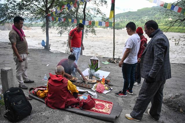 A man (2nd L) sits by the river bank to pray for his son, a missing flash flood victim in Trishuli, in Nepal's Nuwakot district, on September 5, 2026. (Photo by Prakash MATHEMA / AFP)