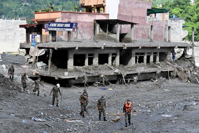 Security and relief personnel walk past a damaged house in the aftermath of flash floods at Trishuli Bazar in Nepal's Nuwakot district on September 5, 2026. Sheltering with relatives or in temporary camps, survivors of devastating floods in Nepal say they can no longer rebuild their homes after the landscape was violently transformed, leaving them focused simply on survival. (Photo by Prakash MATHEMA / AFP)