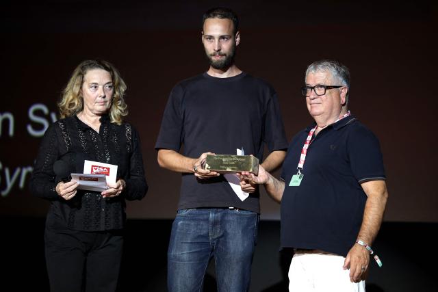 French photographer Philemon Barbier (C) stands by Delphine Lelu (L), co-founder of the Visa festival and André Bonet (R), Deputy Mayor of Perpignan in charge of culture, after receiving the Remi Ochlik prize awarded by the city of Perpignan during the 38th edition of the Visa pour l'image press photography festival in Perpignan, southern France, on September 5, 2026. (Photo by Valentine CHAPUIS / AFP)