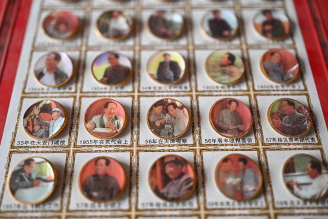 This picture taken on August 18, 2026 shows badges displayed for sale with the image of the late Communist leader Mao Zedong in a shop in Jinzhou. In the ruling Communist Party's telling, Mao remains the revolutionary hero -- his face on banknotes, his portrait overlooking Tiananmen Square, and his body preserved in a mausoleum. (Photo by Pedro PARDO / AFP) / TO GO WITH: China-Mao-anniversary, by Sam DAVIES