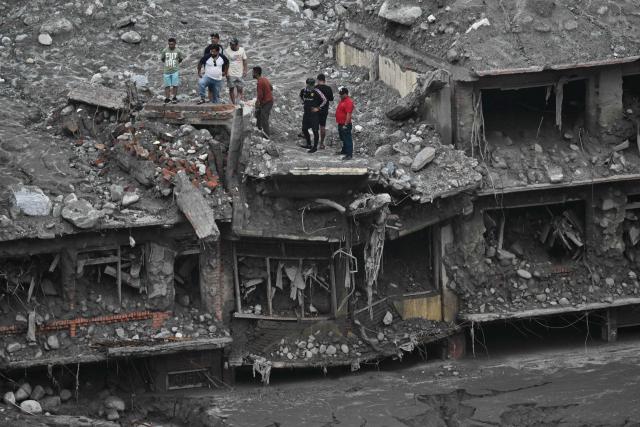 People stand atop damaged houses covered in sludge in the aftermath of flash floods in Trishuli, in Nepal's Nuwakot district on September 6, 2026. The glacial and mountain collapse on the China-Nepal border killed at least 1,384 people and left more than 5,500 missing across the two countries. (Photo by Pedro PARDO / AFP)