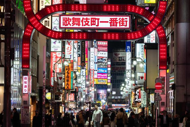(FILES) A man is illuminated as he looks up at a large neon sign in the Shinjuku district in Tokyo on March 30, 2026. Tokyo tourist hotspot Shinjuku will impose a ban on more than half of its holiday rentals including homes on Airbnb, an official said on September 7, 2026, after a surge in complaints about visitors. (Photo by Andrew CABALLERO-REYNOLDS / AFP)