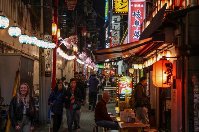 (FILES) People walk past izakaya restaurants in the Shinjuku district in Tokyo on March 30, 2026. Tokyo tourist hotspot Shinjuku will impose a ban on more than half of its holiday rentals including homes on Airbnb, an official said on September 7, 2026, after a surge in complaints about visitors. (Photo by Ludovic MARIN / AFP)