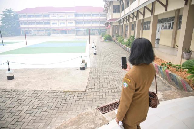 A teacher communicates with students on her phone while standing in the compounds of her school seen shrouded in smog, after local authorities mandated remote learning due to haze from land and forest fires in Pontianak, West Kalimantan, on September 7, 2026. Toxic haze has shrouded parts of Indonesia and Malaysia for weeks as Jakarta struggles to contain fires that have scorched large tracts of Borneo and Sumatra, with the smoke drifting into neighbouring Malaysia, Singapore, and Brunei. (Photo by BAY ISMOYO / AFP)