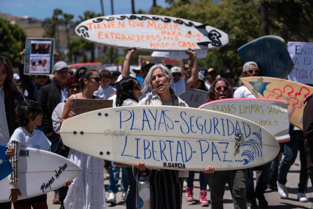 (FILES) A woman holds a surfboard reading "Beaches, Security, Libertad, Peace" next to members of the surfing community protesting against insecurity after two Australians and an American surfers went missing last week during a surfing trip, in Ensenada, Baja California state, Mexico, on May 5, 2024. On September 7, 2026, the trial of the alleged killers of two Australian surfers and one American in 2024 began at the same border resort where the crime took place. Australian brothers Jake and US Callum Robinson were murdered along with Jack Carter in April 2024 on the beaches of Ensenada, located on the Mexican Pacific coast, where the waves are strong and the area is popular with surfers who travel overland from the United States. (Photo by Guillermo Arias / AFP)