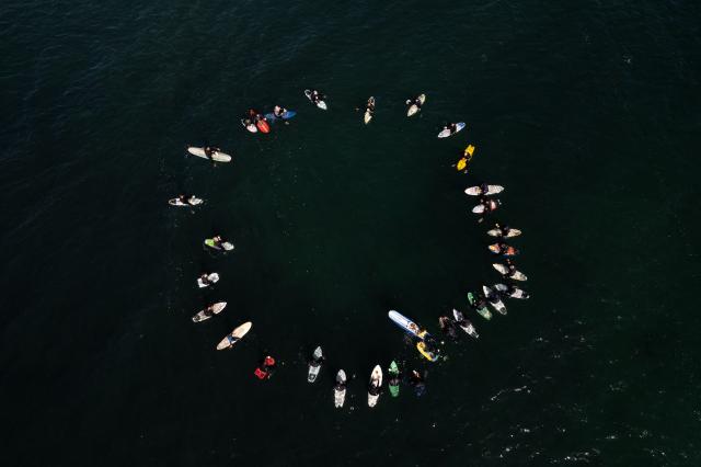 (FILES) Aerial view of surfers taking part in a ceremony in honor of two Australians and an American surfers that went missing last week during a surfing trip at San Miguel Beach in Ensenada, Baja California State, Mexico, on May 5, 2024. On September 7, 2026, the trial of the alleged killers of two Australian surfers and one American in 2024 began at the same border resort where the crime took place. Australian brothers Jake and US Callum Robinson were murdered along with Jack Carter in April 2024 on the beaches of Ensenada, located on the Mexican Pacific coast, where the waves are strong and the area is popular with surfers who travel overland from the United States. (Photo by Guillermo Arias / AFP)