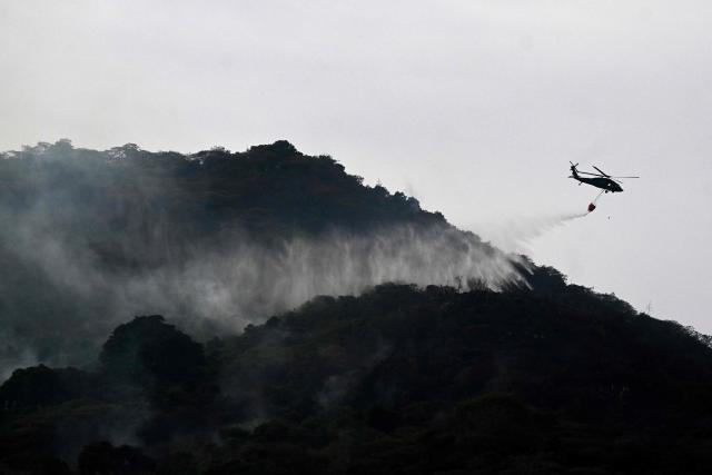A Colombian Air Force helicopter with a bambi bucket drops water to fight a wildfire at Cerro Gordo in Yumbo, Valle del Cauca department, Colombia on September 7, 2026. (Photo by JOAQUIN SARMIENTO / AFP)