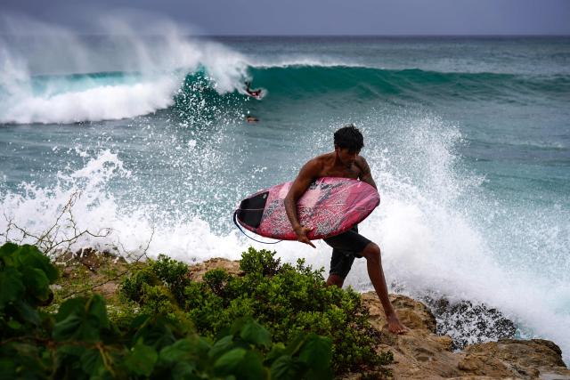 A surfer carries his board along the shoreline at Electric Beach in Waianae, Hawaii, on September 7, 2026. A hurricane warning was issued September 7 for the westernmost Hawaiian islands of Kauai and Niihau as Category 3 Hurricane Lowell approached the US Pacific island chain, the National Hurricane Center (NHC) said. The core of Lowell was expected to pass just west of Niihau on the night of September 7 or early on September 8, the center said in its latest bulletin released at 8 am Hawaii time (1800GMT). (Photo by Michelle Bir / AFP)