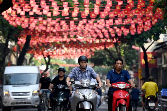 Commuters ride beneath Party and national flags in Hanoi on September 8, 2026. (Photo by Nhac NGUYEN / AFP)