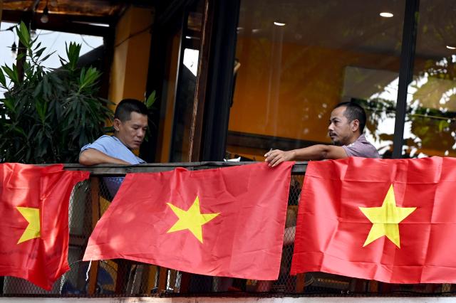 Men sit drinking coffee beside national flags in Hanoi on September 8, 2026. (Photo by Nhac NGUYEN / AFP)