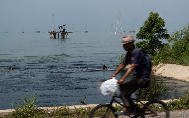 A man rides a bicycle in front of abandoned oil wells in Maracaibo lake, Zulia state, Venezuela on September 7, 2026. Venezuela and US signed an agreement granting US access to more than 65 billion barrels -- almost 20 percent -- of oil in Venezuela, which holds the largest proven reserves in the world. (Photo by John Chacón / AFP)